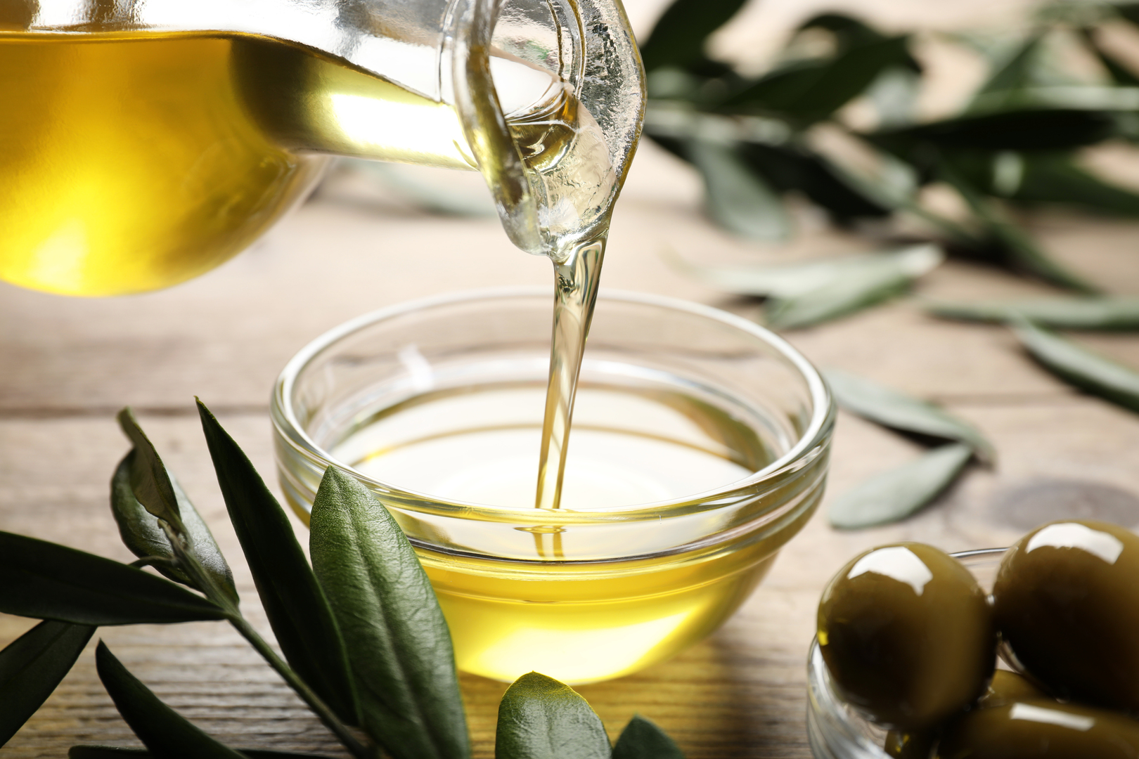 Olive oil being poured from a glass jug into a bowl.