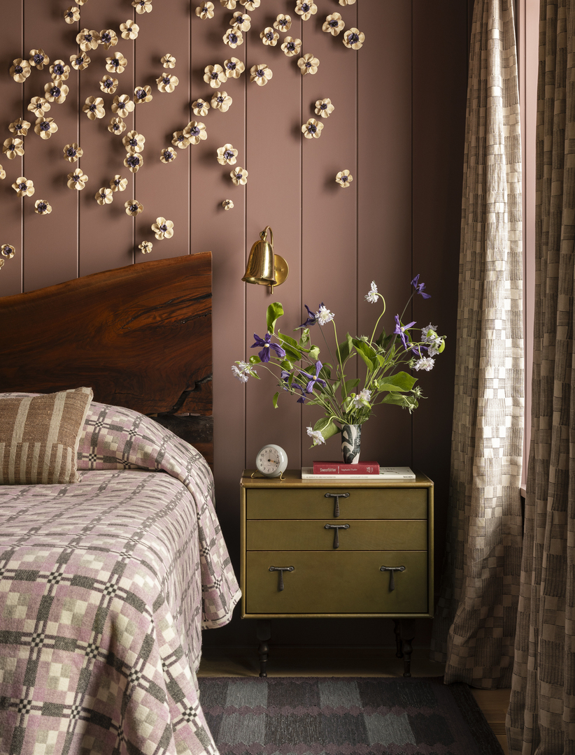 Bedroom with mauve walls, ceramic flower wall art, and a live flower arrangement on a nightstand.