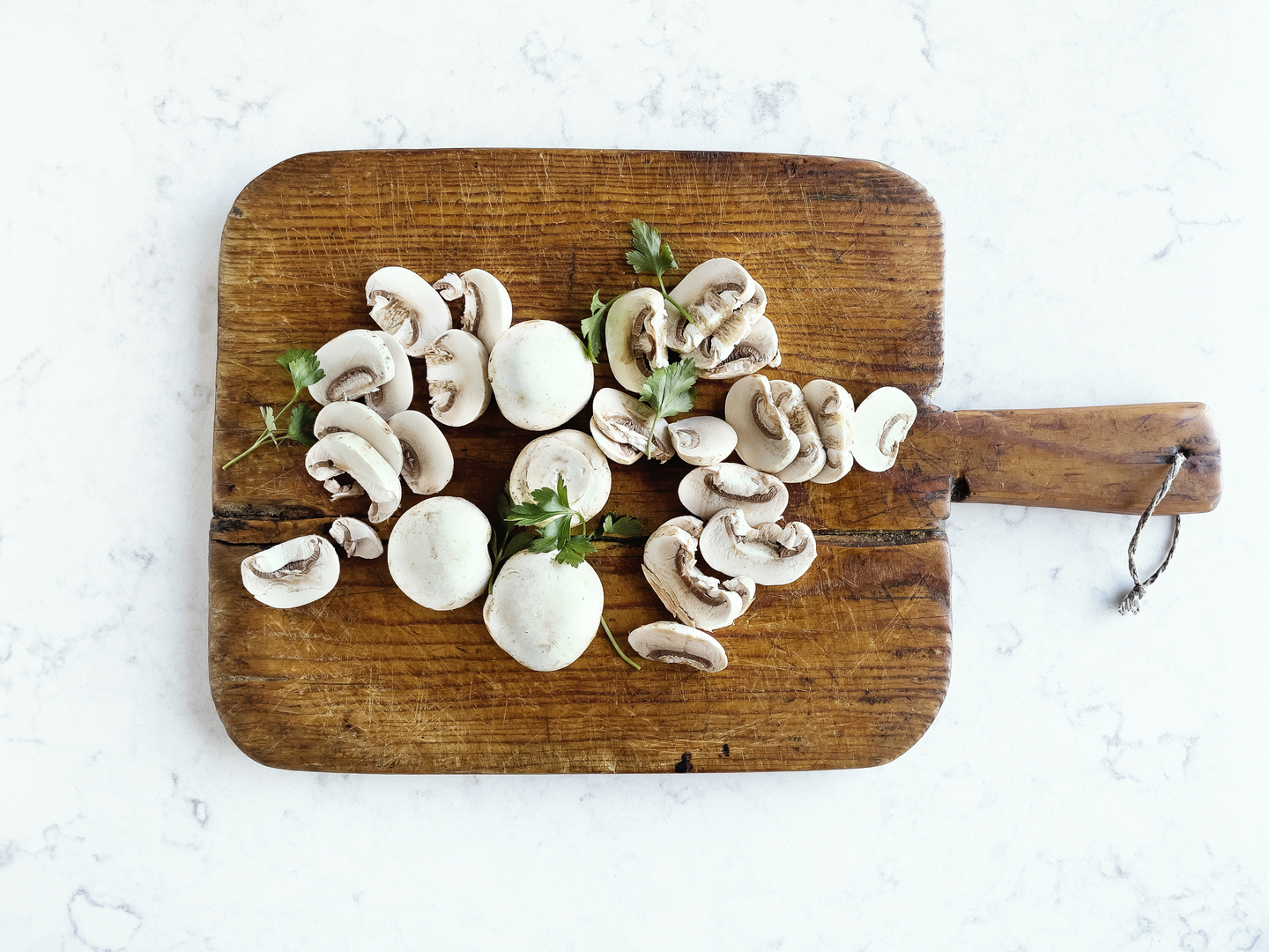 Sliced white button mushrooms on a wooden cutting board.