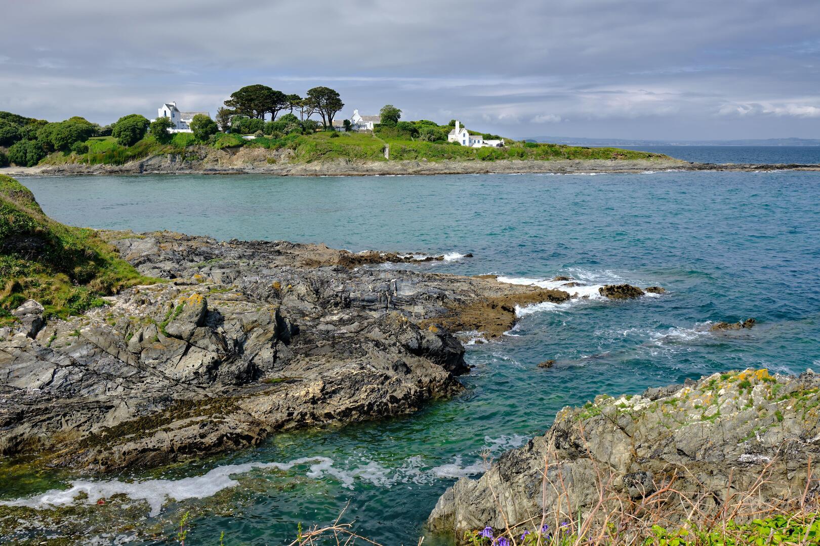 Coastal view of Chapel Point in Cornwall, England, with white houses on a hill overlooking the sea.