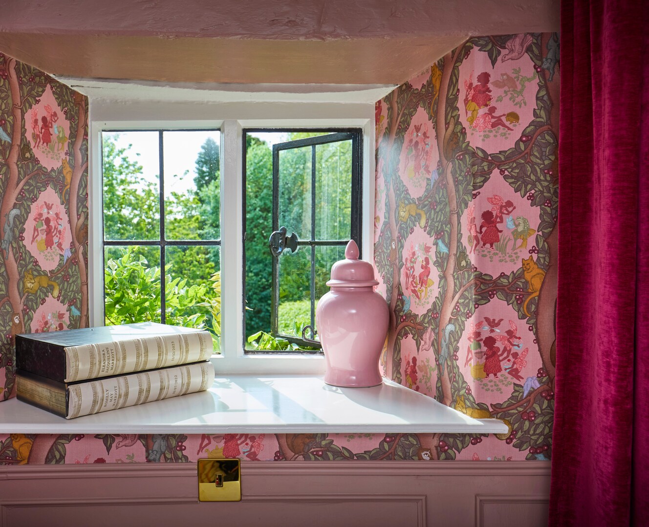Window seat with books, a pink jar, and whimsical wallpaper.